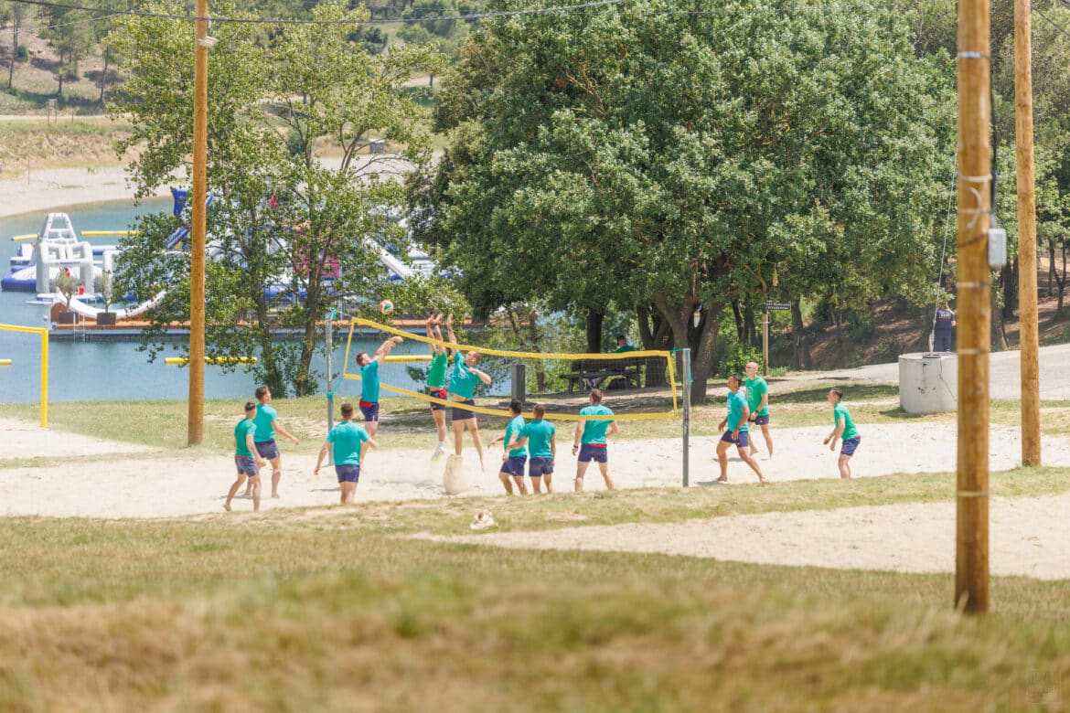 Match de volley-ball sur sable au Lac de la Cavayère à Carcassonne, ambiance estivale entre amis avec les structures gonflables de l’aquapark en arrière-plan.
