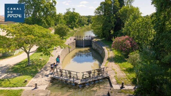 Écluse sur le Canal du Midi à Carcassonne, bordée de verdure avec des promeneurs et cyclistes profitant d’une belle journée ensoleillée.
